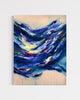 An abstract canvas painting featuring dynamic, textured brushstrokes of deep blue, navy, and white, accented with splashes of yellow, red, and purple, set against a light beige background. The painting is shown hanging on a neutral light gray wall.
