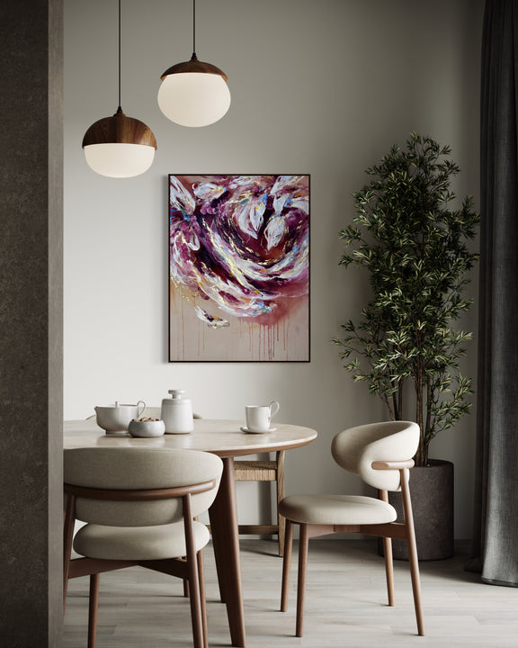 An abstract painting with swirling purple, pink, white, and gold brushstrokes hanging on a light gray wall in a modern dining room setting with a wooden table, chairs, pendant lights, and a potted plant.