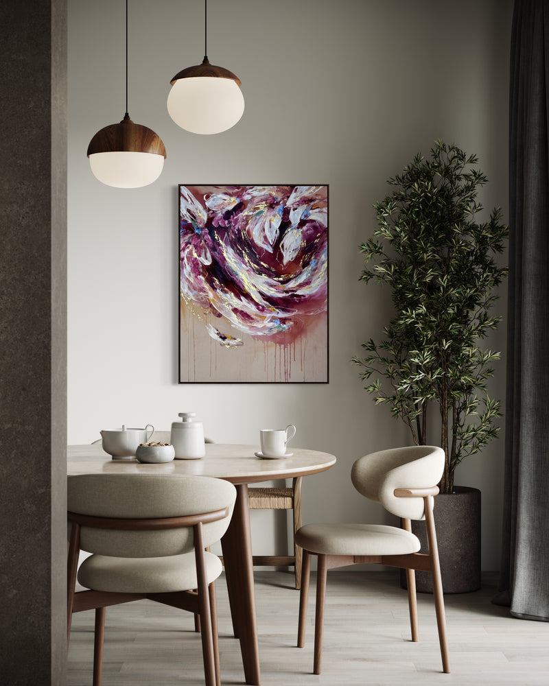 An abstract painting with swirling purple, pink, white, and gold brushstrokes hanging on a light gray wall in a modern dining room setting with a wooden table, chairs, pendant lights, and a potted plant.