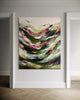 An abstract canvas painting with sweeping green, beige, white, and pink brushstrokes, displayed on a white wall in a hallway with light wood herringbone flooring.